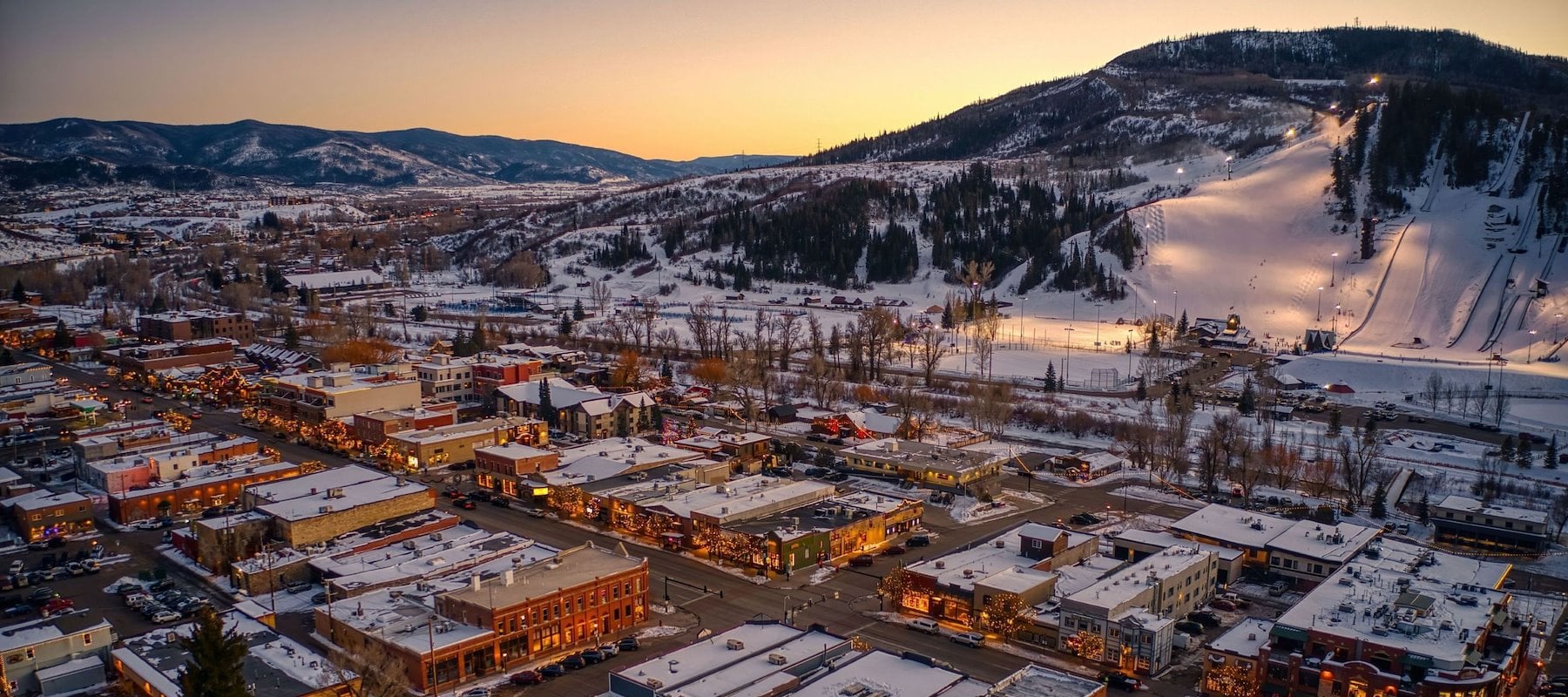 An aerial view of a snowy town with buildings and mountains in the background.